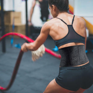 Female athlete using battle ropes wearing a back support belt